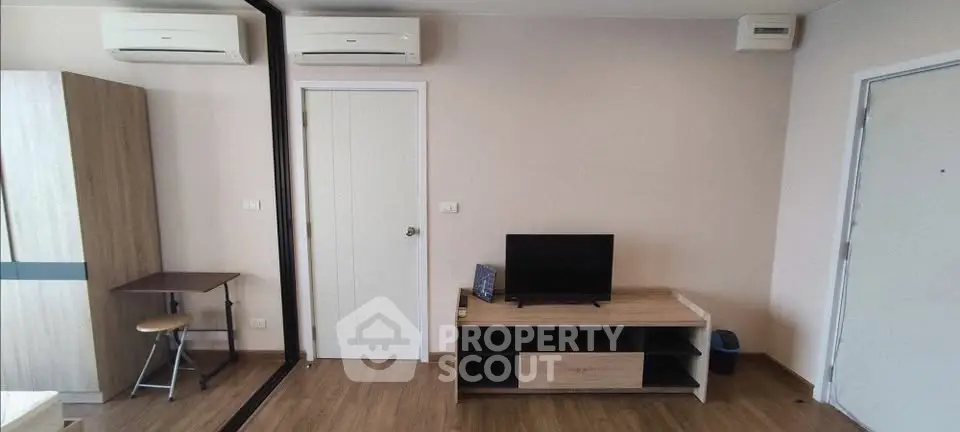 Modern living room with air conditioning and wooden flooring, featuring a TV stand and compact workspace.