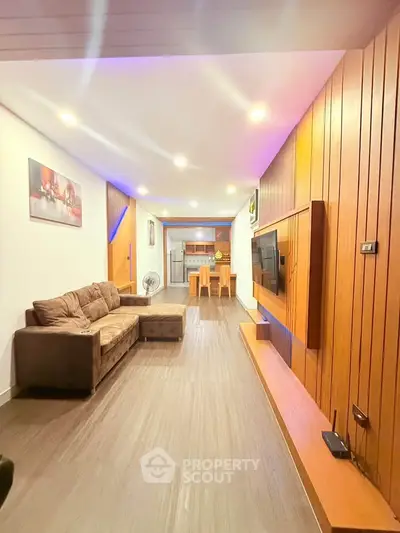 Modern living room with wooden paneling and open layout leading to dining area.