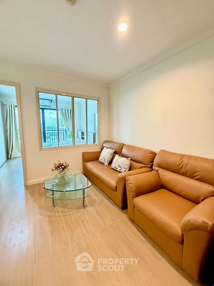 Cozy living room with leather sofas and glass coffee table, featuring a bright window view.