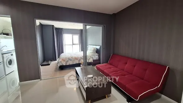 Modern apartment interior with red sofa and view into cozy bedroom