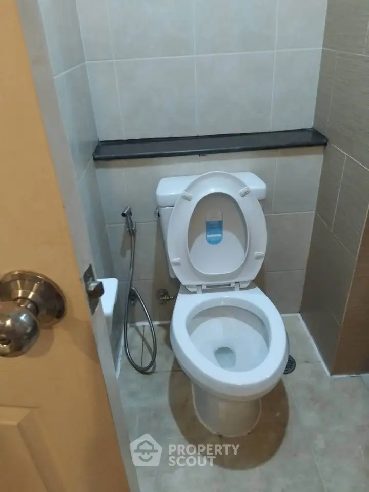 Compact bathroom with modern toilet and bidet spray, featuring neutral tile design.