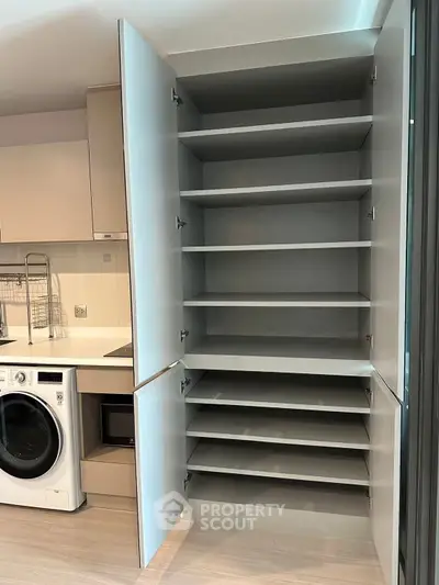 Modern kitchen with open storage cabinet and washing machine, showcasing sleek design and functionality.