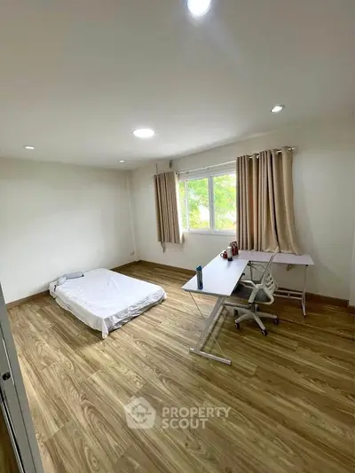 Spacious minimalist bedroom with wooden flooring and large window view.