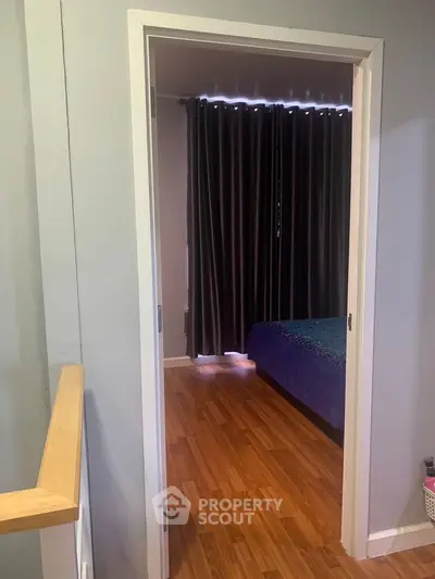 Cozy bedroom with wooden flooring and dark curtains, perfect for relaxation.