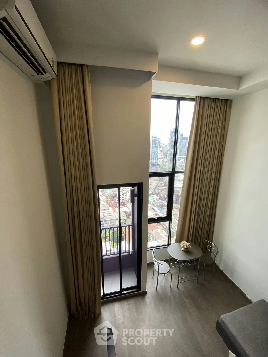 Modern high-rise apartment with floor-to-ceiling windows and city view, featuring a cozy dining area and balcony.