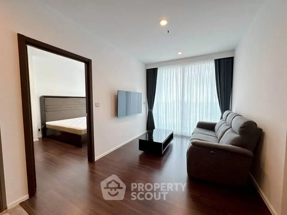 Modern living room with sleek furniture and large window, adjacent to a cozy bedroom.
