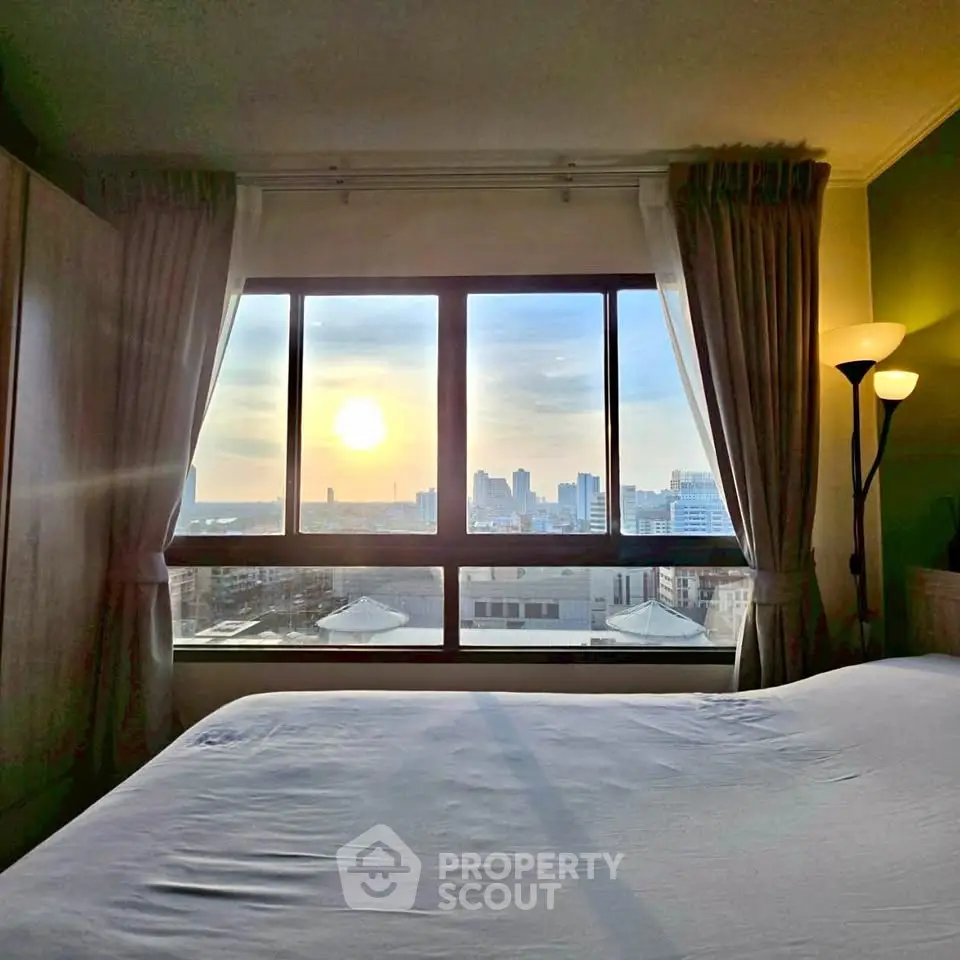 Cozy bedroom with stunning city view through large window at sunset.