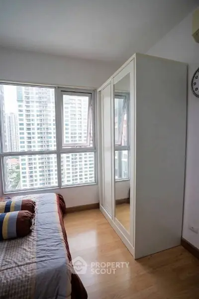 Modern bedroom with large windows and city view, featuring a sleek wardrobe and cozy bed setup.