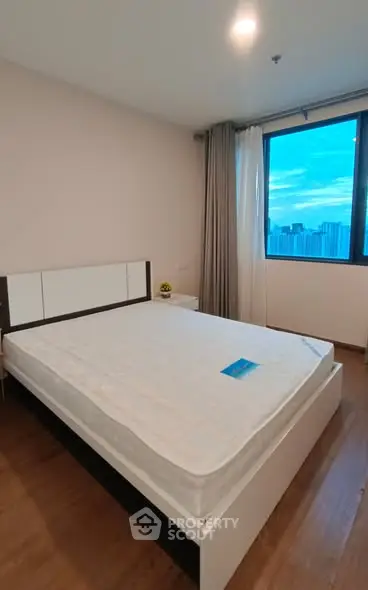 Spacious bedroom with large window offering stunning city views, modern furnishings, and ample natural light.