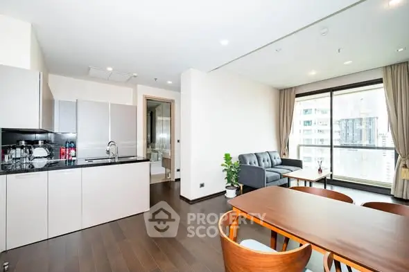 Modern open-plan living room with kitchen in a high-rise apartment, featuring sleek furniture and large windows.