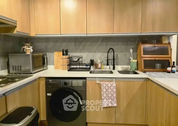 Modern kitchen with wooden cabinets, washing machine, and sleek appliances.