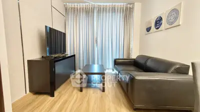 Modern living room with sleek black leather sofa and flat-screen TV, featuring elegant decor and natural light.