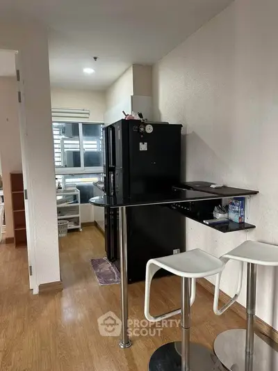 Modern kitchen with sleek bar stools and black refrigerator in cozy apartment.