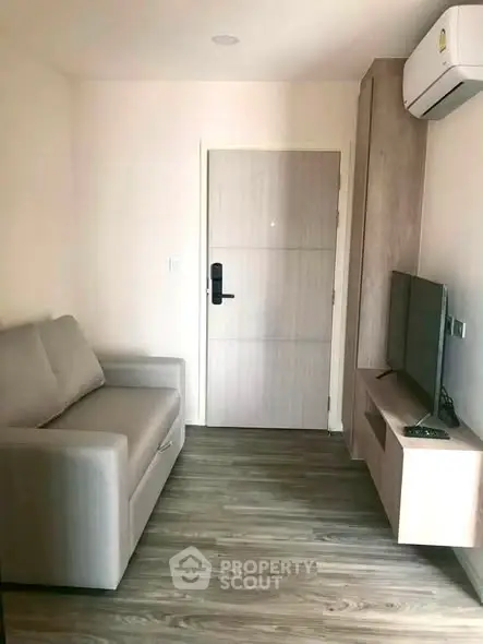 Cozy living room with modern sofa and wall-mounted TV, featuring sleek wooden flooring and air conditioning.