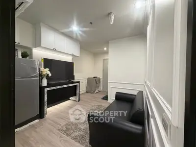 Modern living room with sleek black sofa, stylish decor, and open kitchen layout in a contemporary apartment.