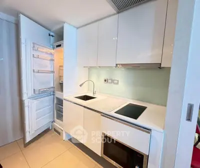 Modern kitchen with sleek white cabinets, built-in appliances, and open fridge showcasing contemporary design.