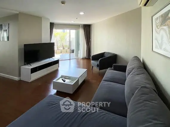 Spacious living room with modern furniture and large TV, opening to a balcony with natural light.