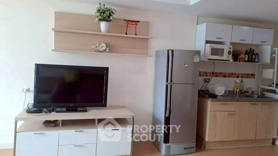 Modern living room with TV, fridge, and kitchen area in open layout apartment.