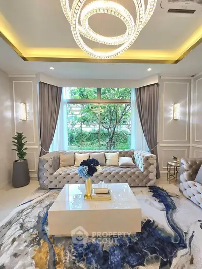 Luxurious living room with elegant chandelier and plush sofas, featuring a large window with garden view.