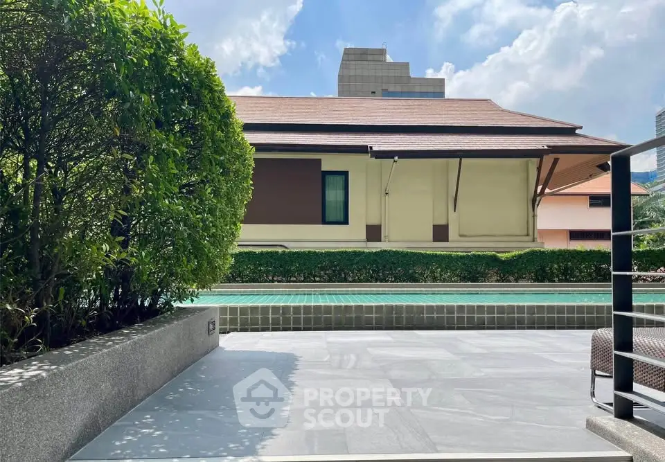 Luxurious poolside view with lush greenery and modern architecture under a clear blue sky.