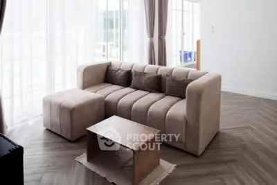Modern living room with stylish beige sofa and wooden coffee table, featuring large windows and elegant curtains.