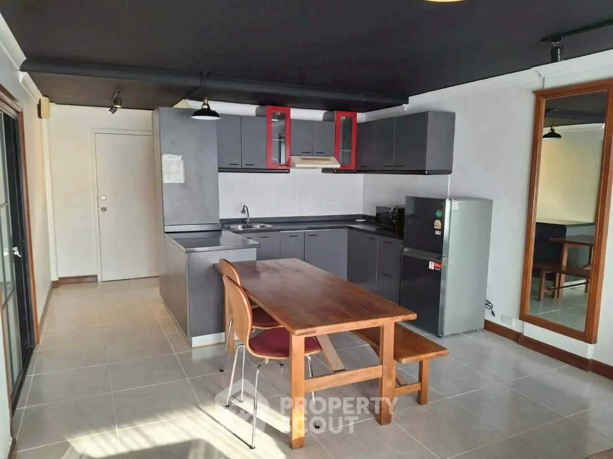 Modern kitchen with sleek cabinets and dining area, featuring a large mirror and natural light.