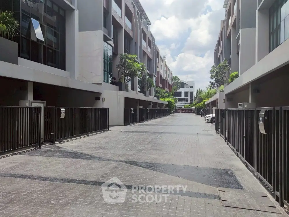 Modern townhouse complex with gated entrance and paved driveway under a clear sky.