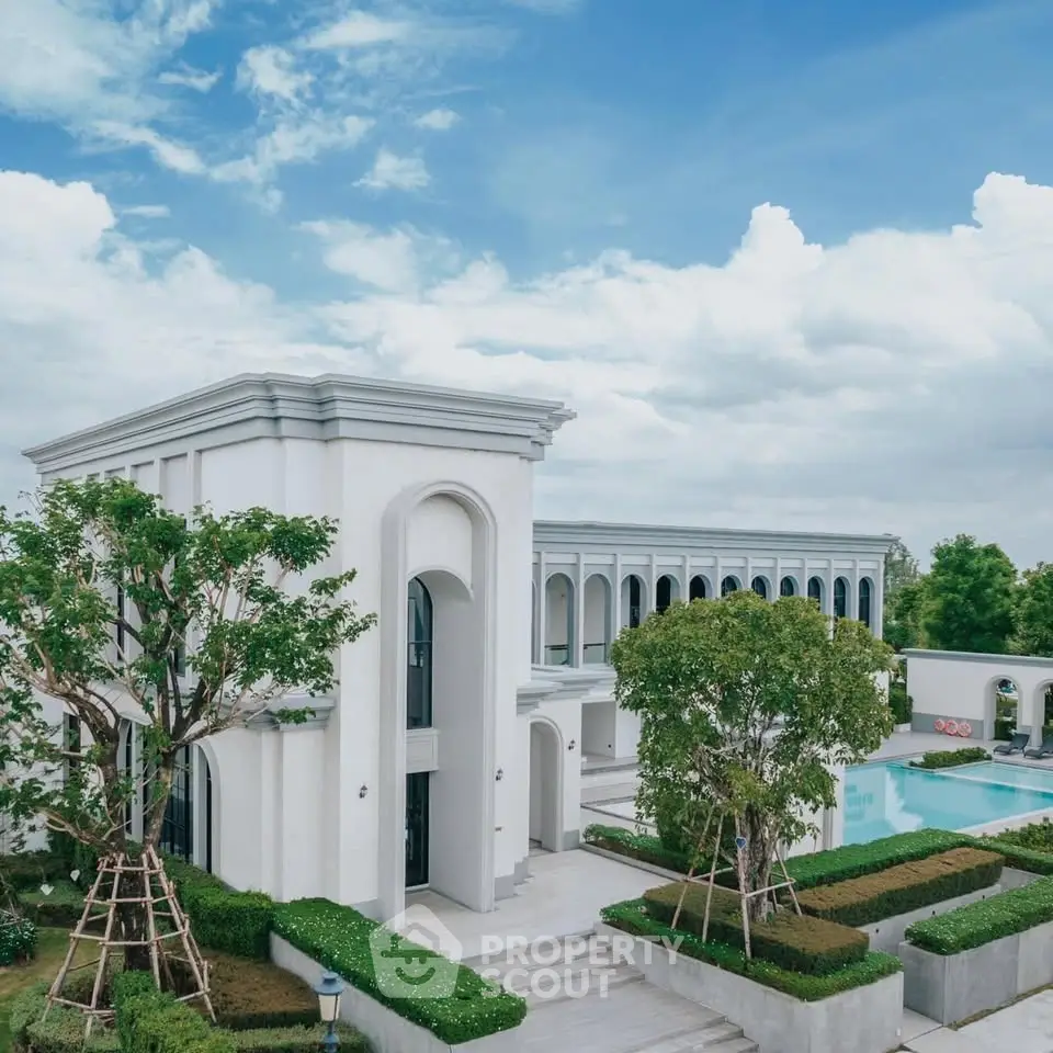 Luxurious modern villa with stunning architecture and private pool, surrounded by lush greenery and clear blue skies.