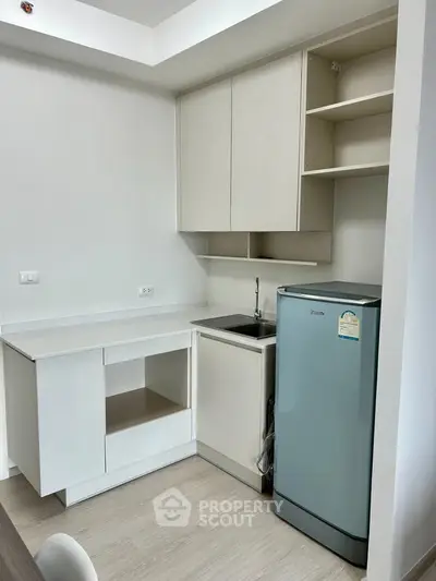 Modern compact kitchen with sleek cabinetry and stainless steel fridge in a stylish apartment.
