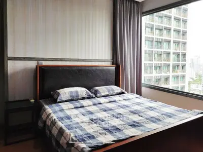 Modern bedroom with large window offering city view, featuring stylish bed and contemporary decor.