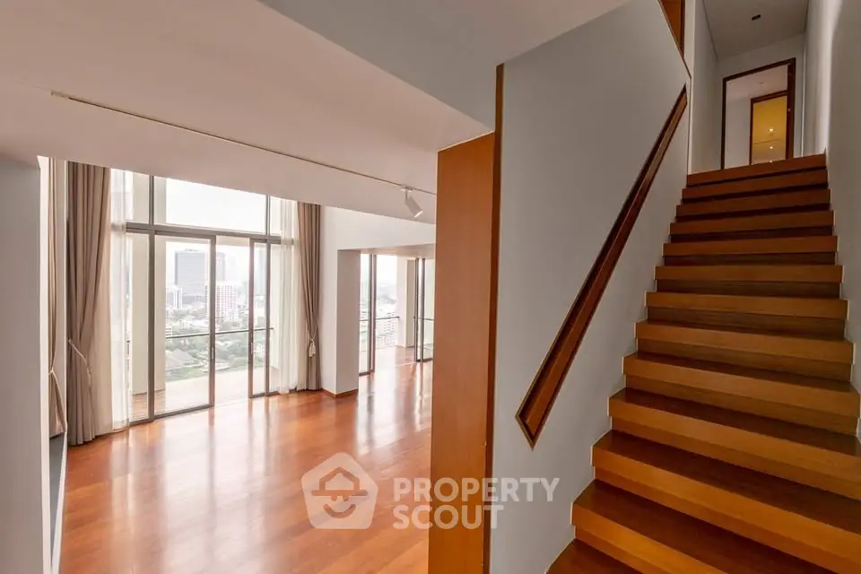 Spacious modern living room with wooden floors and large windows offering city views.
