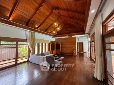 Spacious living room with wooden ceiling and floor, featuring modern furniture and large windows.