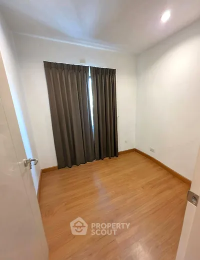 Spacious empty room with wooden flooring and large window with curtains, perfect for customization.