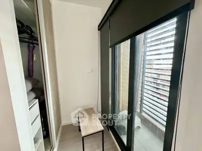 Modern bedroom with large window and closet, featuring sleek blinds and minimalist furniture.