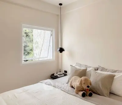 Cozy bedroom with plush bedding and modern pendant light, featuring a large window with garden view.