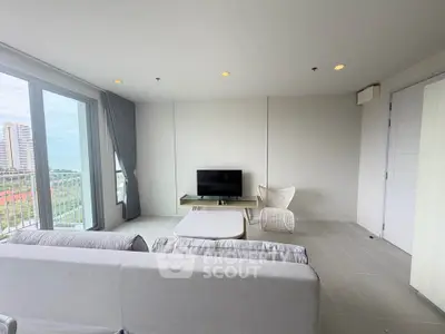 Modern living room with large windows and city view, featuring minimalist furniture and neutral tones.
