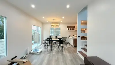 Modern open-plan living room with dining area and staircase, featuring sleek design and natural light.