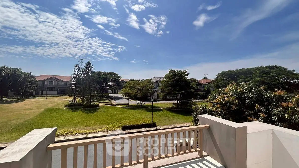 Stunning view from a balcony overlooking lush greenery and elegant homes under a clear blue sky.