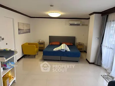 Spacious bedroom with modern decor and natural light, featuring a cozy seating area and air conditioning.