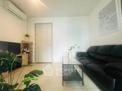 Modern living room with sleek black sofa, glass coffee table, and minimalist decor.