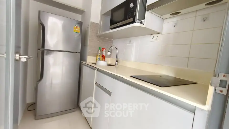 Modern compact kitchen with stainless steel fridge and microwave in sleek apartment.