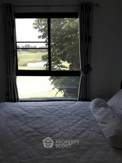 Cozy bedroom with scenic window view of lush greenery and golf course.