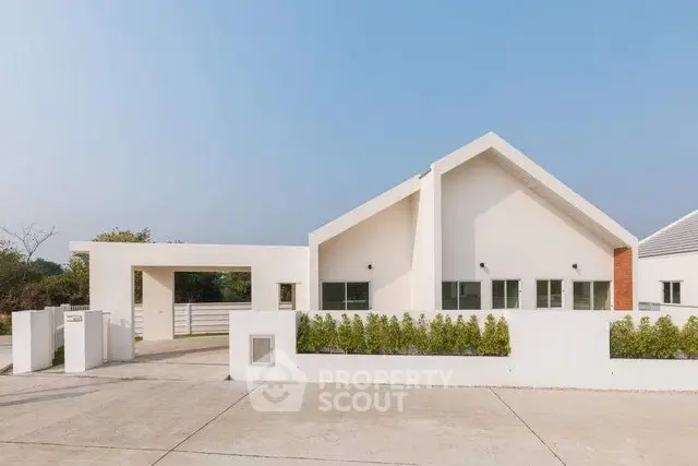 Modern minimalist house exterior with clean lines and white facade, featuring a spacious driveway and lush greenery.