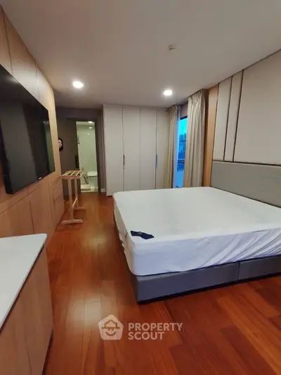 Spacious bedroom with wooden flooring and modern furnishings, featuring a large bed and built-in wardrobe.