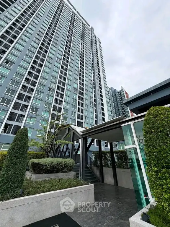 Modern high-rise building exterior with lush landscaping and sleek entrance.