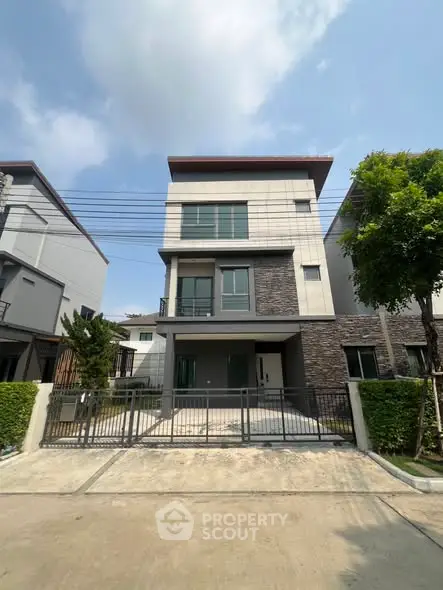 Modern three-story house with sleek design and spacious driveway in suburban neighborhood.