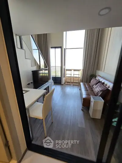 Modern loft-style living room with high ceilings and large windows, featuring a cozy leather sofa and dining area.