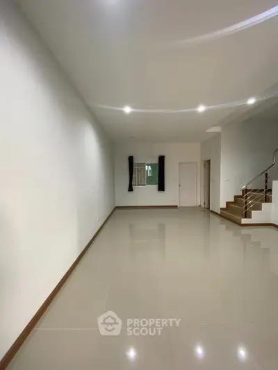 Spacious and well-lit living room with glossy tiled flooring, recessed lighting, and an elegant staircase leading to the upper level, perfect for modern living.