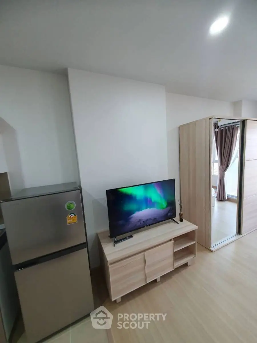 Modern apartment interior with TV and fridge, showcasing sleek design and natural light.