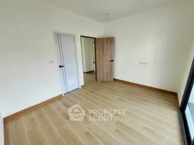 Spacious empty room with wooden flooring and large window, perfect for customization.